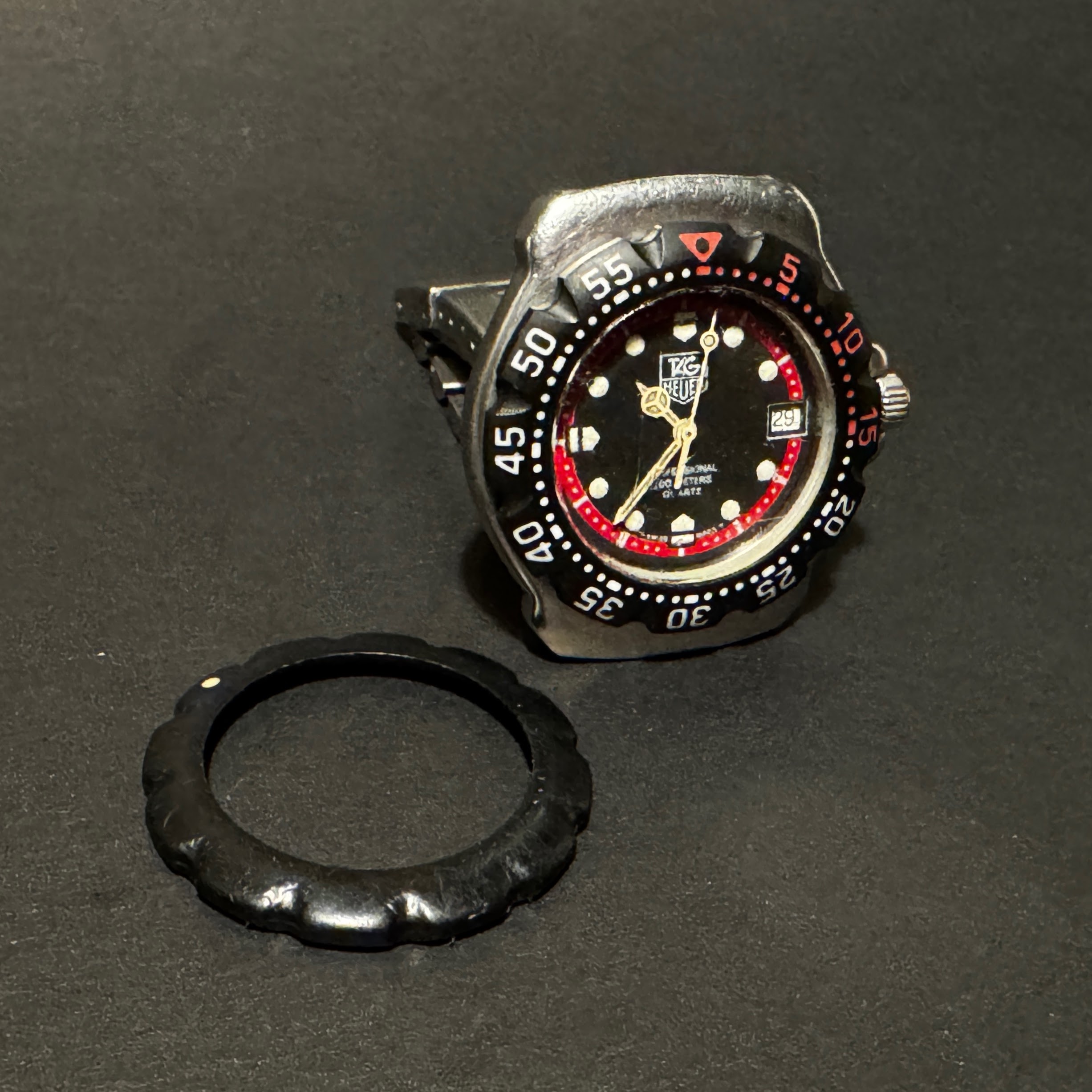 Before and after the repair: the replacement bezel is now on the watch, with the old removed bezel laid out on the table for comparison.